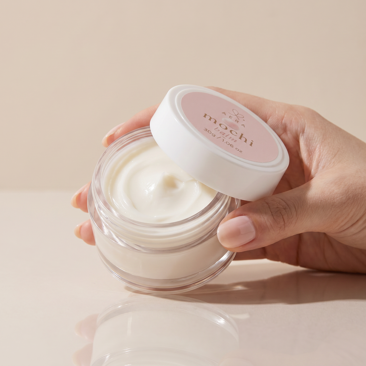 Opened glass balm jar with creamy white balm and white snap lid in hand